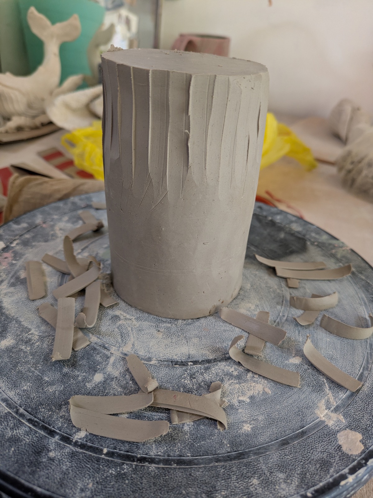 The cylinder on the wheel with vertical carved lines, clay shavings scattered around